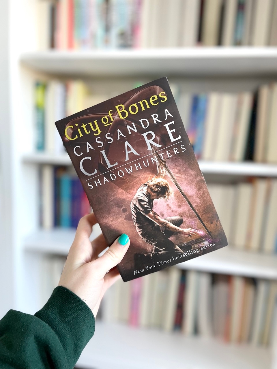 Front cover of the fantasy novel City of Bones by Cassandra Clare in front of a bookcase